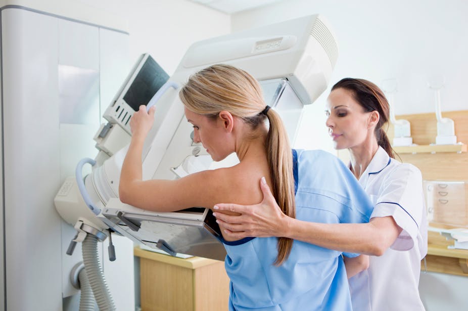 Une femme est en train de faire une mammographie, avec l'aide d'une autre femme professionnelle de santé.