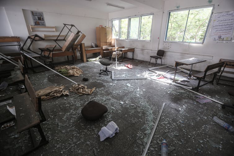 A classroom is seen with desks turned upside down and glass on the floor.