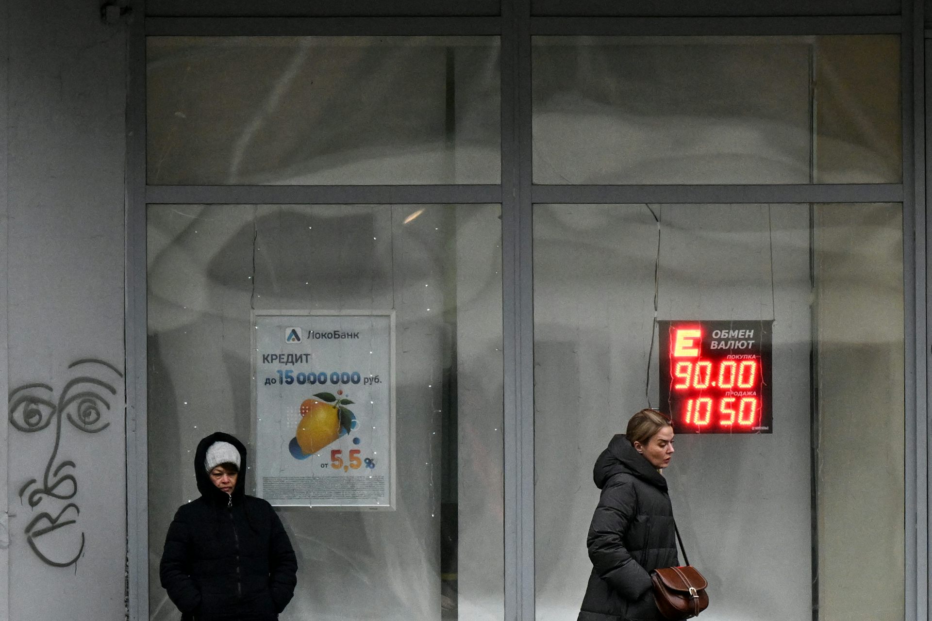 Two people stand outside a glass building with currency figures in neon.