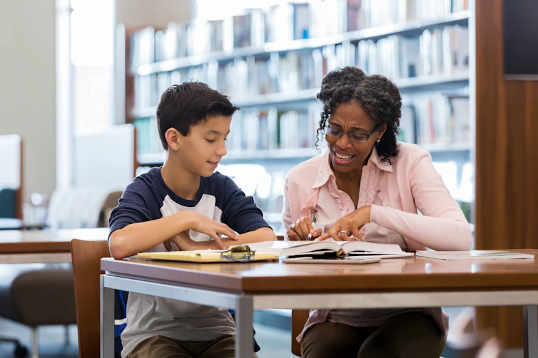 A woman tutors a young student in a library.
