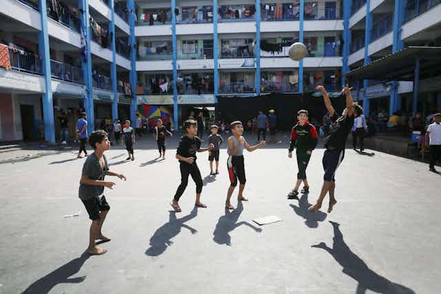 Young boys play with a ball in a large school courtyard. 