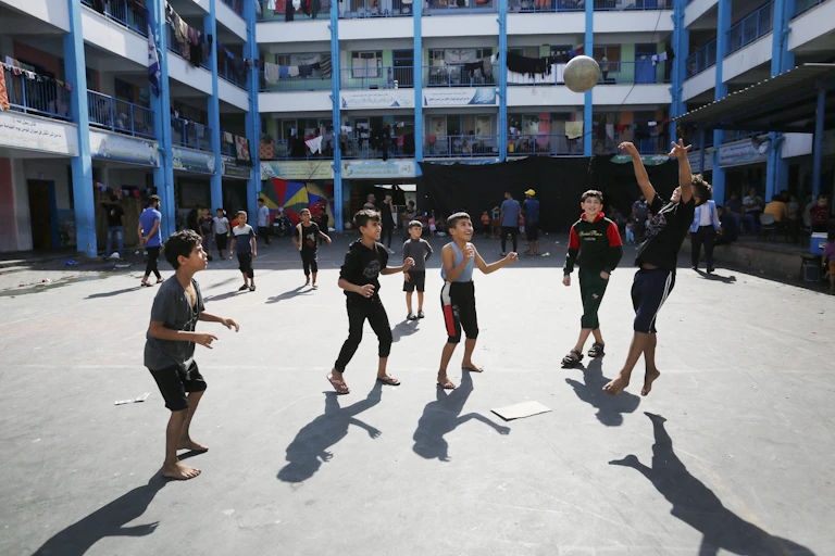Young boys play with a ball in a large school courtyard.