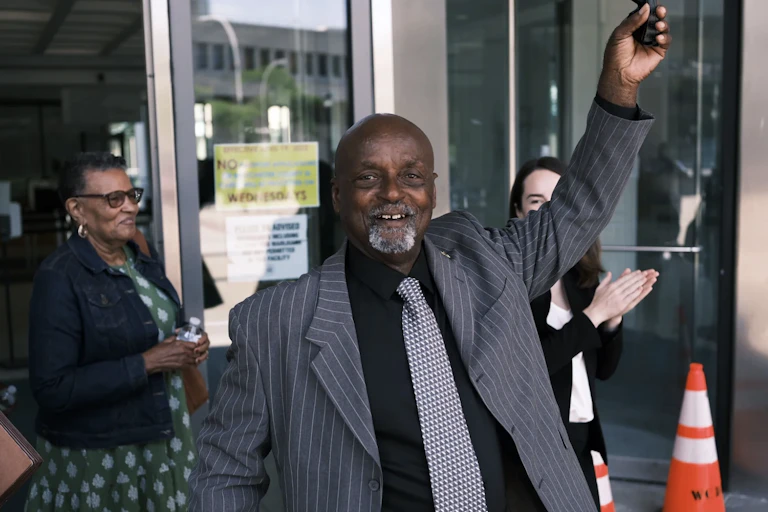 A man in a suit smiles with one arm up in the air in victory