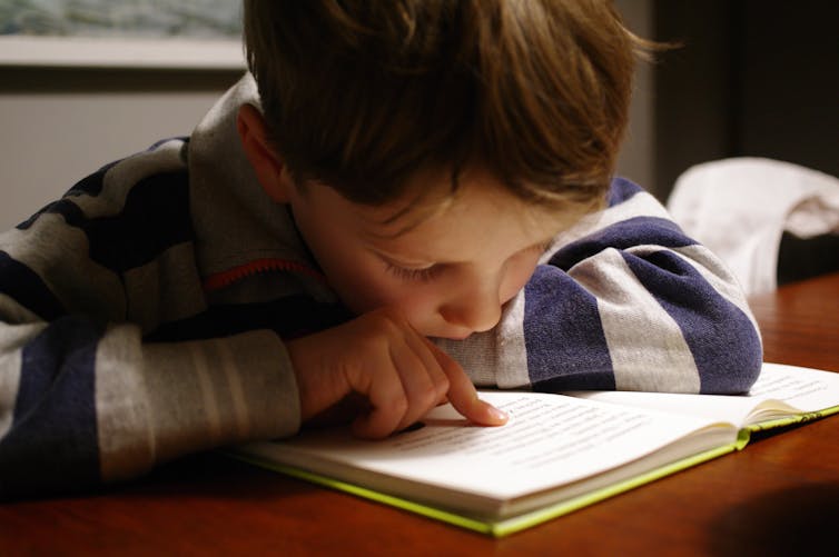 A young boy reads a book, using his finger as a guide.