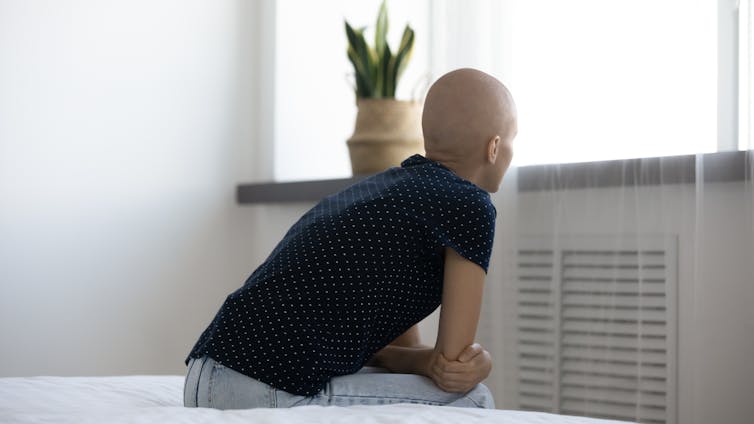 A person with a bald head sitting on a bed.