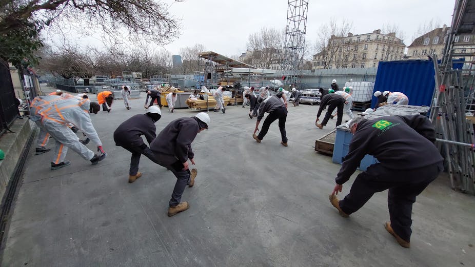 Sur un chantier du BTP, des travailleurs sont penchés en avant. Ils sont en train de pratiquer des exercices physiques.