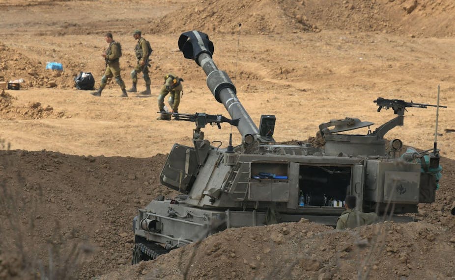 An Israeli tank with three soldiers behind it in desert-like surroundings.