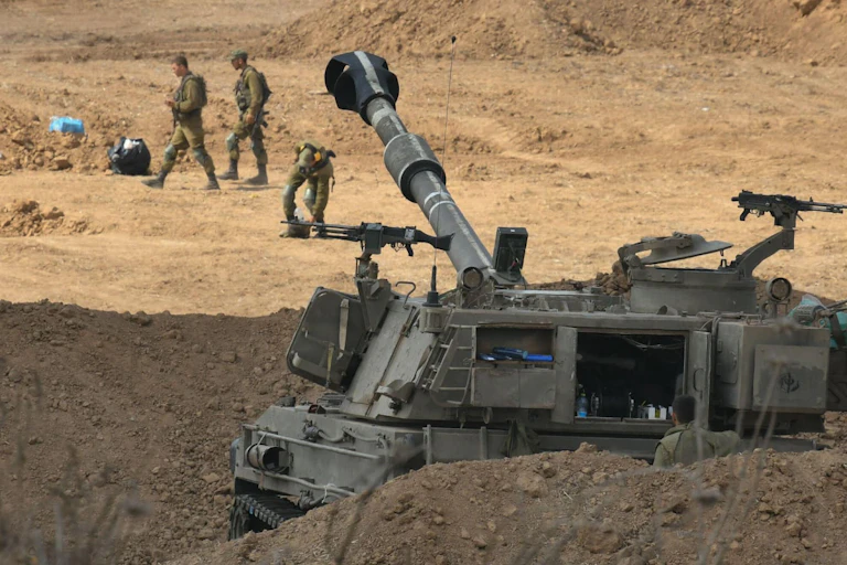 An Israeli tank with three soldiers behind it in desert-like surroundings.