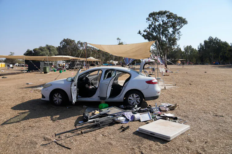 A car with no windows sits in front a tree at a former music festival site.