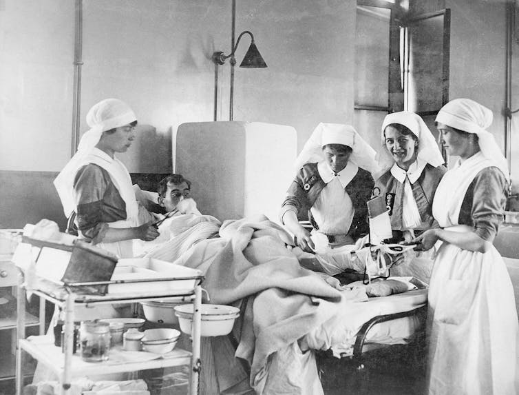 Archival photograph in black and white of nurses in a hospital with a patient during the first world war.