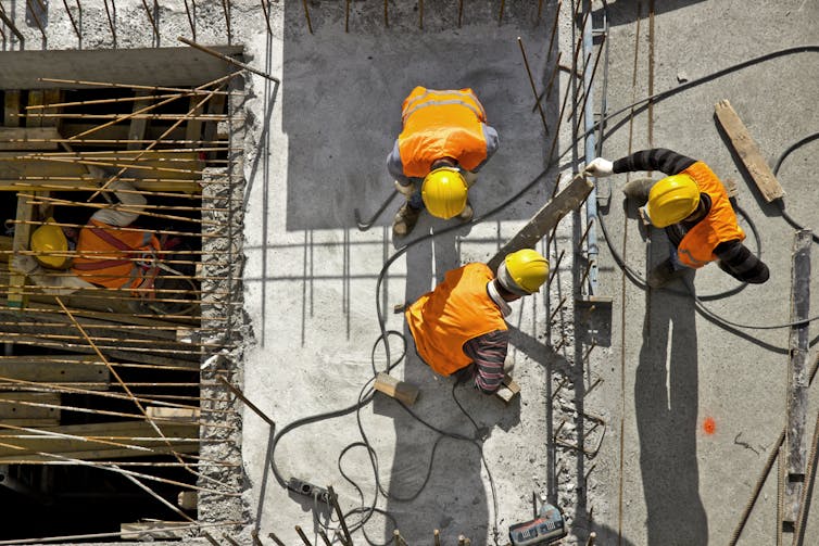 Three construction workers in hardhats and orange vests seen from above