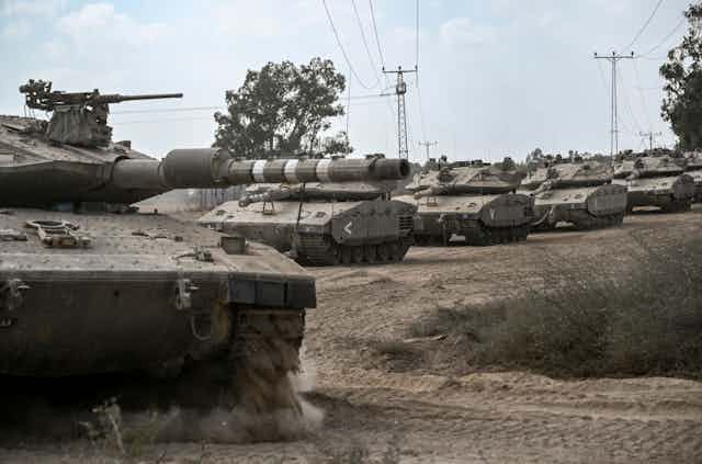 A line of tanks roll down a dirt road.