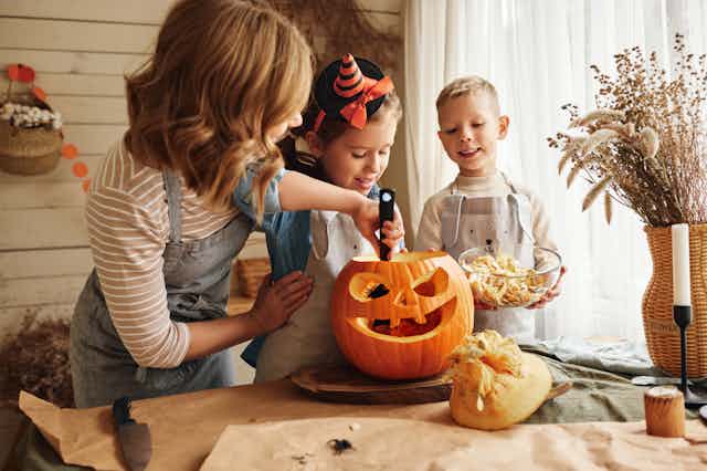 A mother and two kids carving a pumpkin for Halloween.