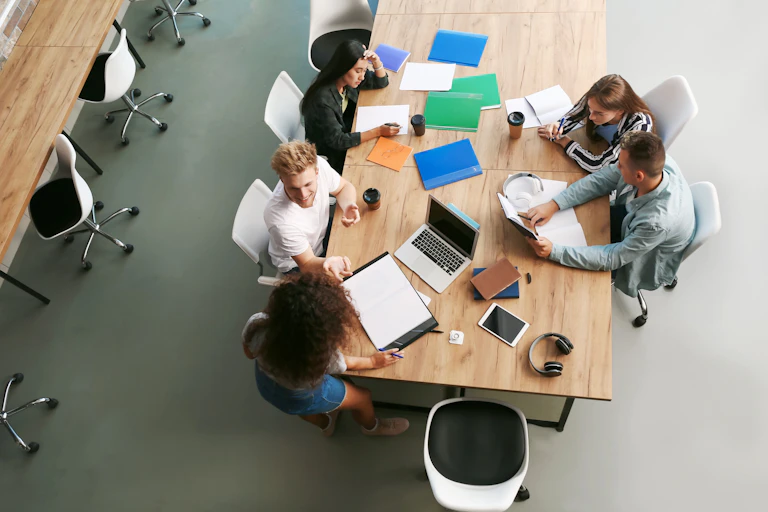Visión aérea de un grupo de estudiantes trabajando, estudiando y hablando alrededor de una mesa.