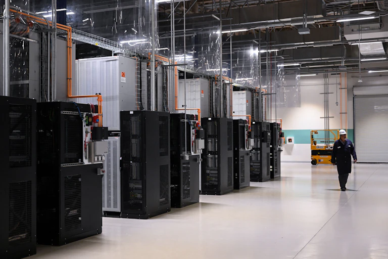 A worker walks past a row of large metal cases connected by pipes and wires
