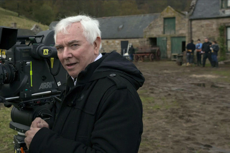 Terence Davies in a field with a film camera.