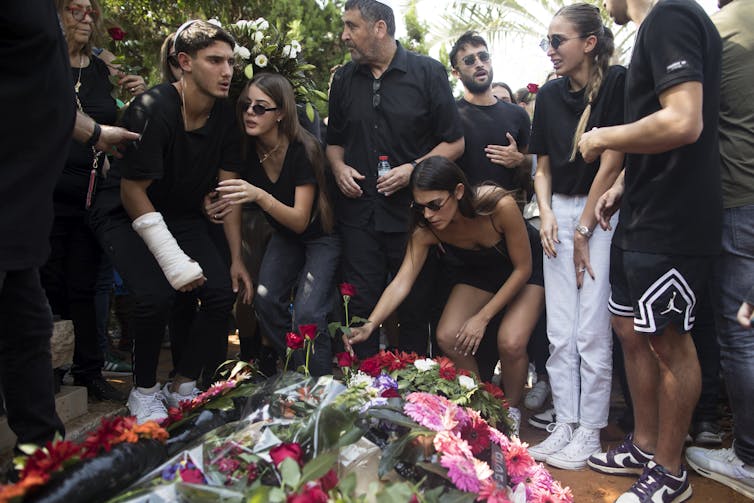Mourners crying and placing flowers at a grave site.