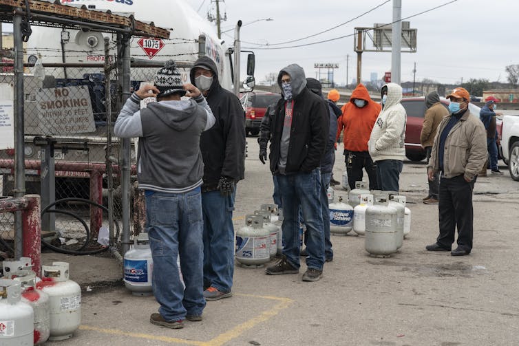 People wait at a propane gas station, bundled in heavy clothes.