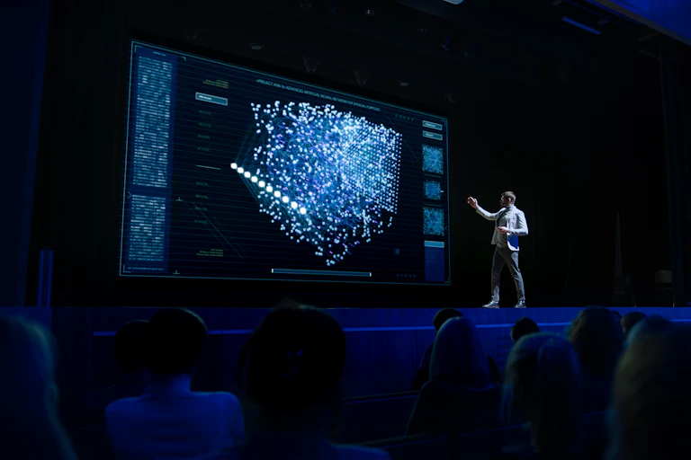a man stands on a stage and a screen behind him shows a scattergraph
