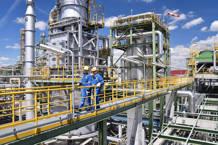 two people in safety gear walk outdoors through a factory
