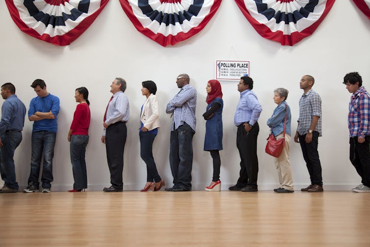 With a red, white and blue banner above them, a diverse group of Americans stand in line to vote.