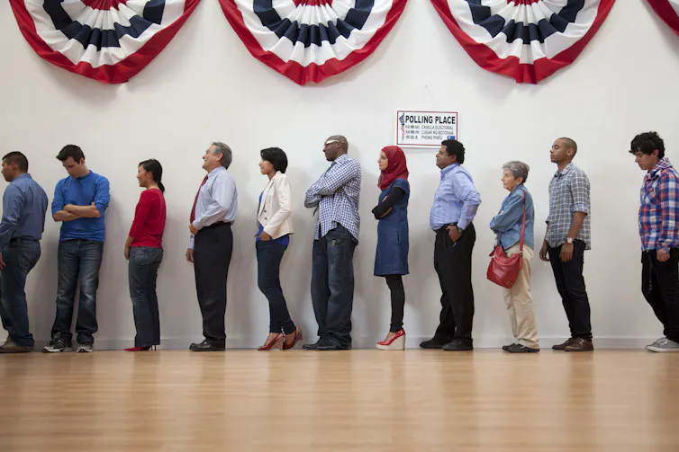 With a red, white and blue banner above them, a diverse group of Americans stand in line to vote.
