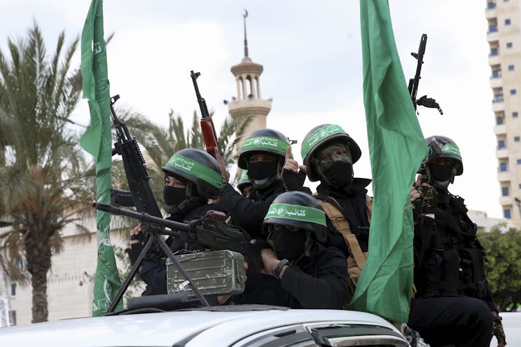 Masked men in black hold aloft rifles.