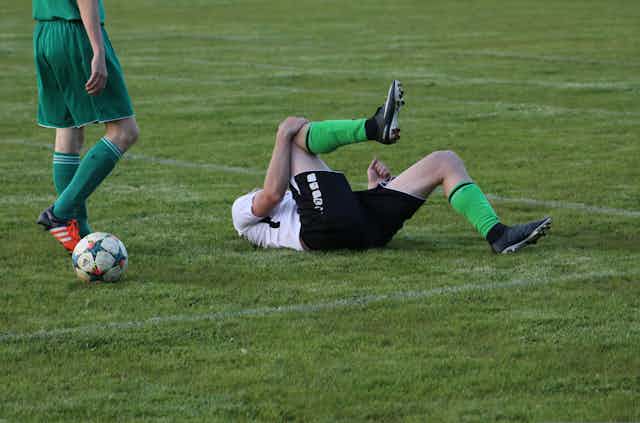 Photo d’un footballer qui se tient le genou, allongé sur le dos