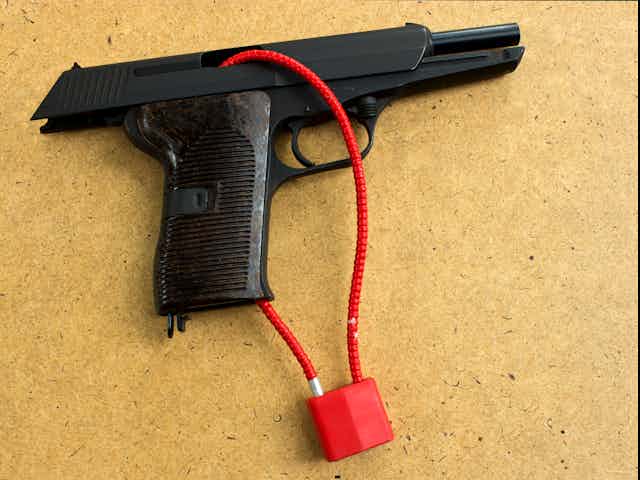 A firearm is seen with a red cable lock tied around it.