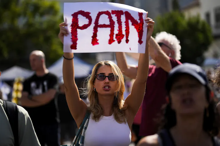 A woman holds up a sign that says PAIN
