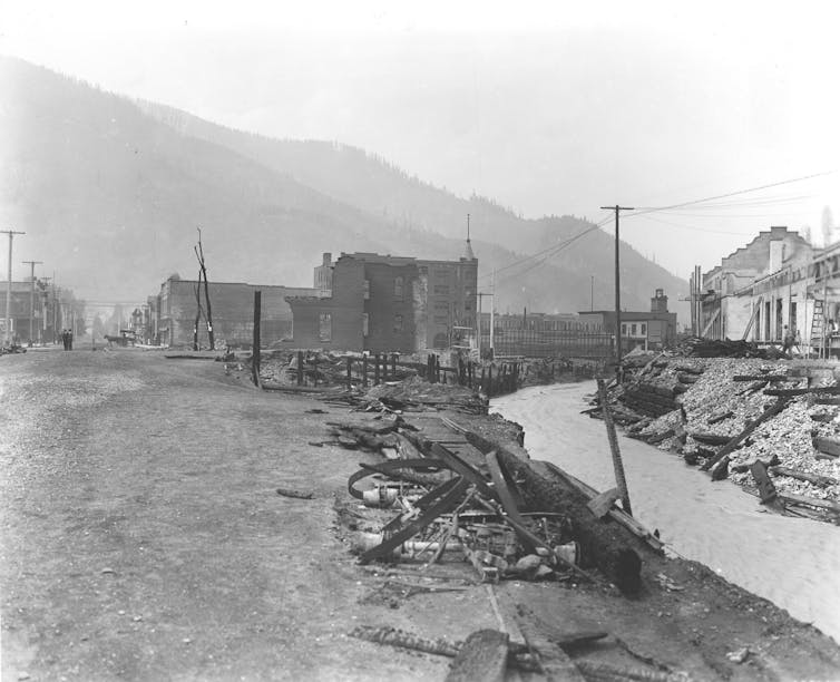 A black and white photo from 1910 shows rail lines and the burned shells of buildings