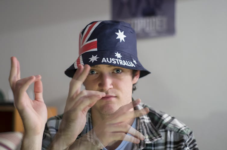 A photo of a man in an Australian flag hat waving his hand in front of his face.