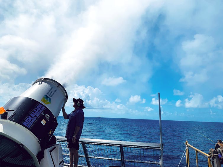 Photo of the latest cloud brightening generator (V model) in action, on board a vessel, with a person standing alongside it. The cannon is about as tall as the person.