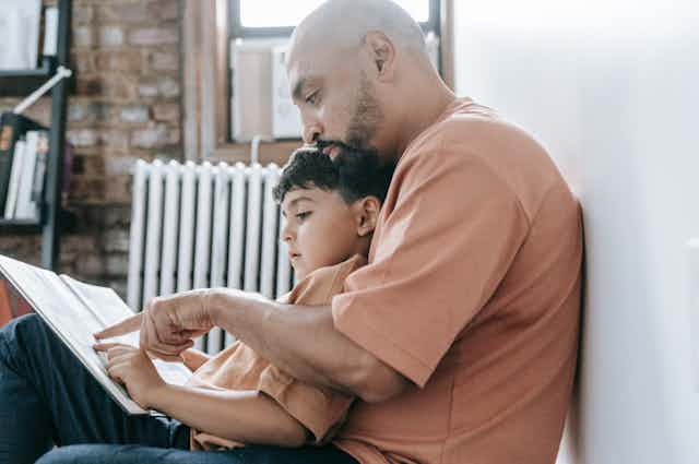 A man sits with a young boy, reading a book.