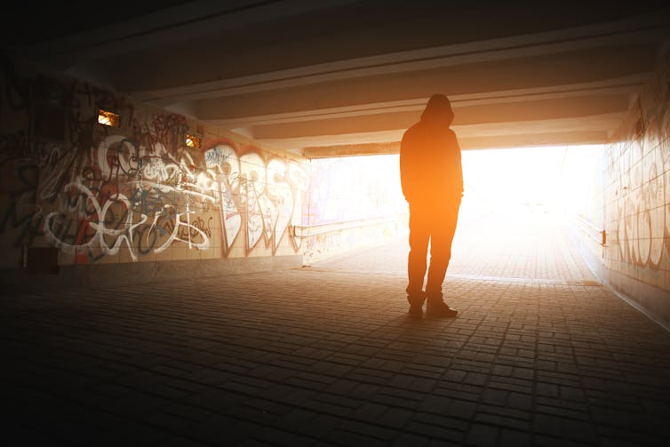 young person stands in underpass with graffiti on wall