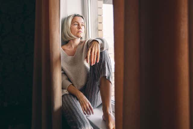 woman sits by window looking sad