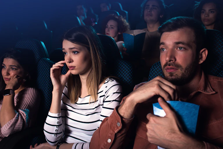 Three young adults watch a movie in a movie theatre.