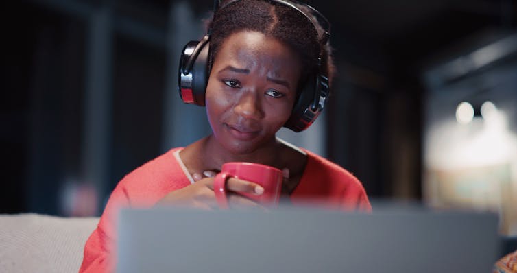 A young woman wearing headphones watches a movie or show on her laptop.