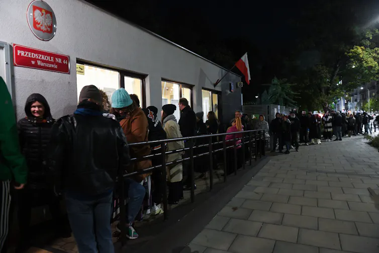 A long queue of people standing outside a polling station in the dark.