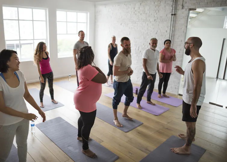 Groupe de personnes écoutant les instructions d’un entraîneur pendant une session d’activité physique en salle.