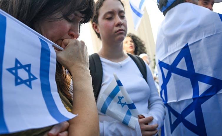 Women look sad while holding Israeli flags.