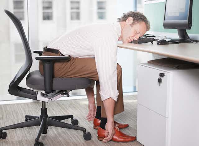 A white-collar professional sleeps at his workstation, resting his head on the keyboard.