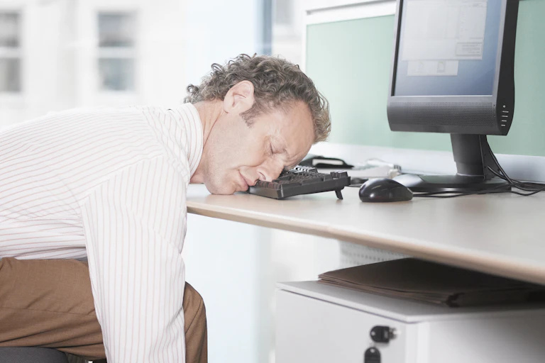 A white-collar professional sleeps at his workstation, resting his head on the keyboard.