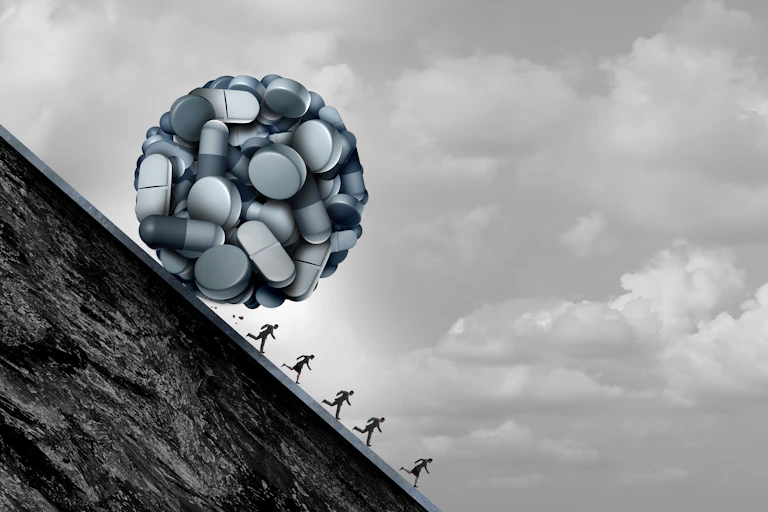 Black and white illustration of a ball of pills rolling down a hill, about to roll over small human figures