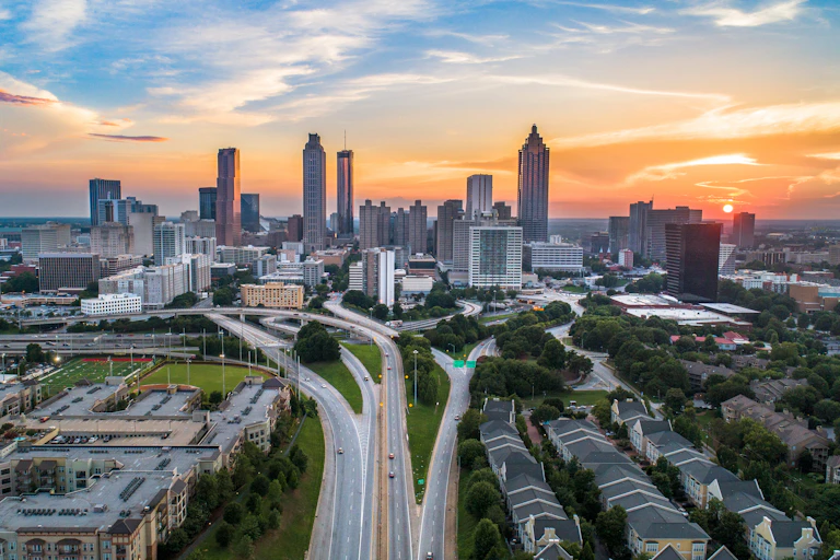 The sun sets over the Atlanta skyline, with a smattering of single-family houses visible in the foreground.