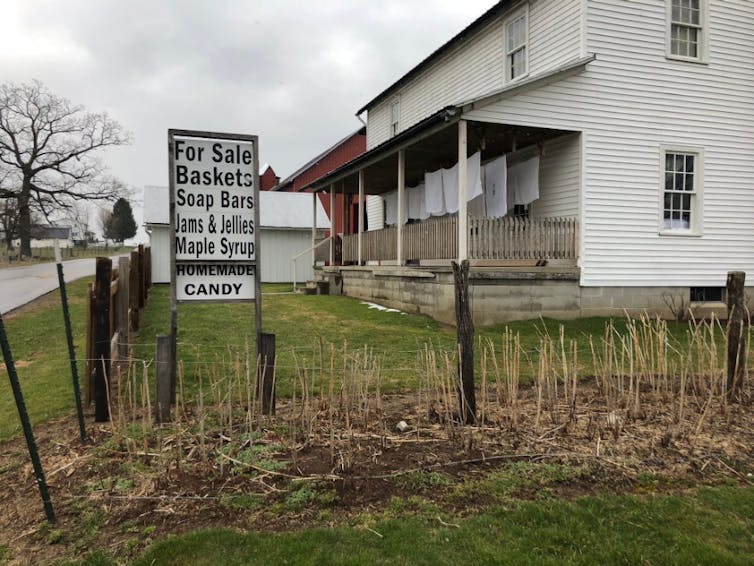 A simple sign advertising homemade goods and candy outside a white farmhouse.