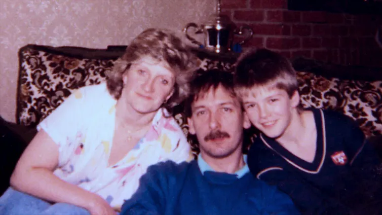 An old photo of a woman, a man and a young boy on a couch, looking at the camera