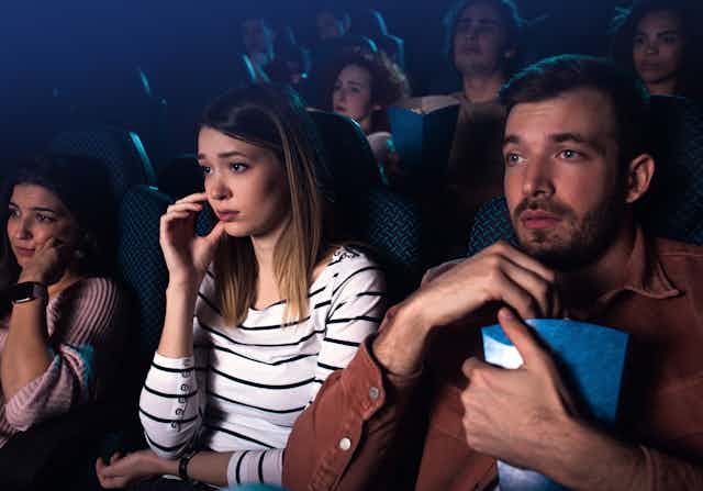 Tres jóvenes adultos ven una película en un cine.