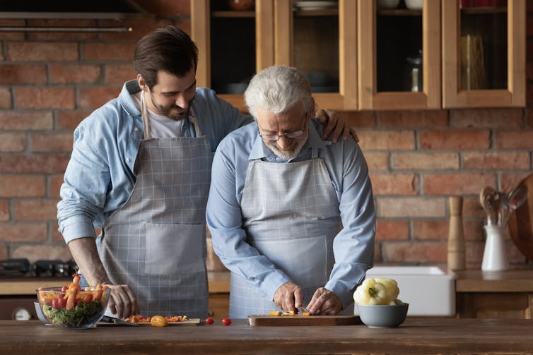 A young man with a senior man chopping vegetables in the kitchen.