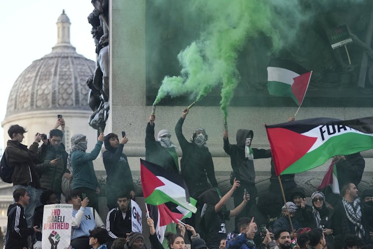 Pro-Palestinian protesters hold flares billowing green smoke and wave Palestinian flags.